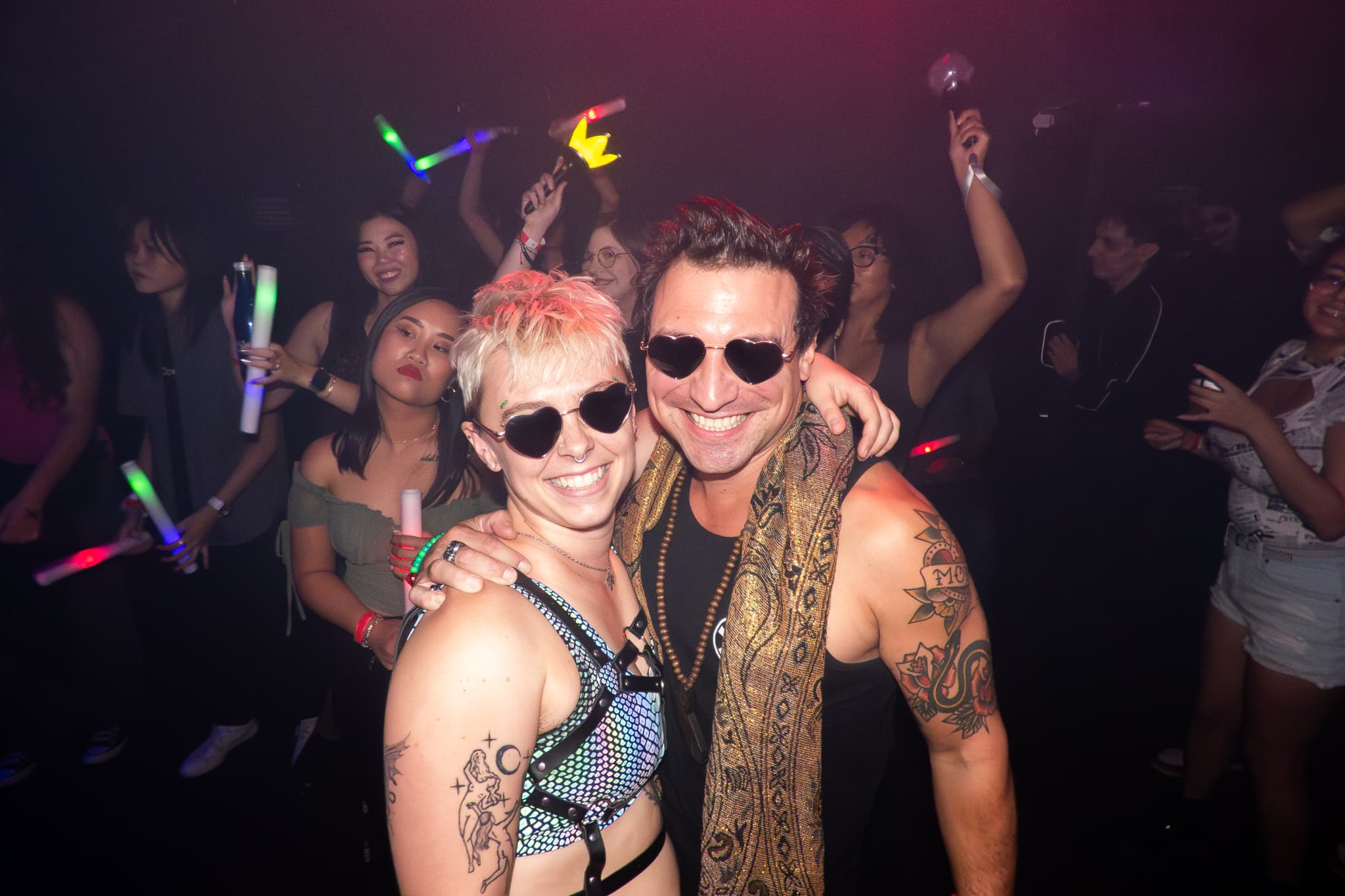 Event photography by Chase Tipton - Photo of two people embracing closely and smiling, in front of a crowd of people at a club, people dancing in the background